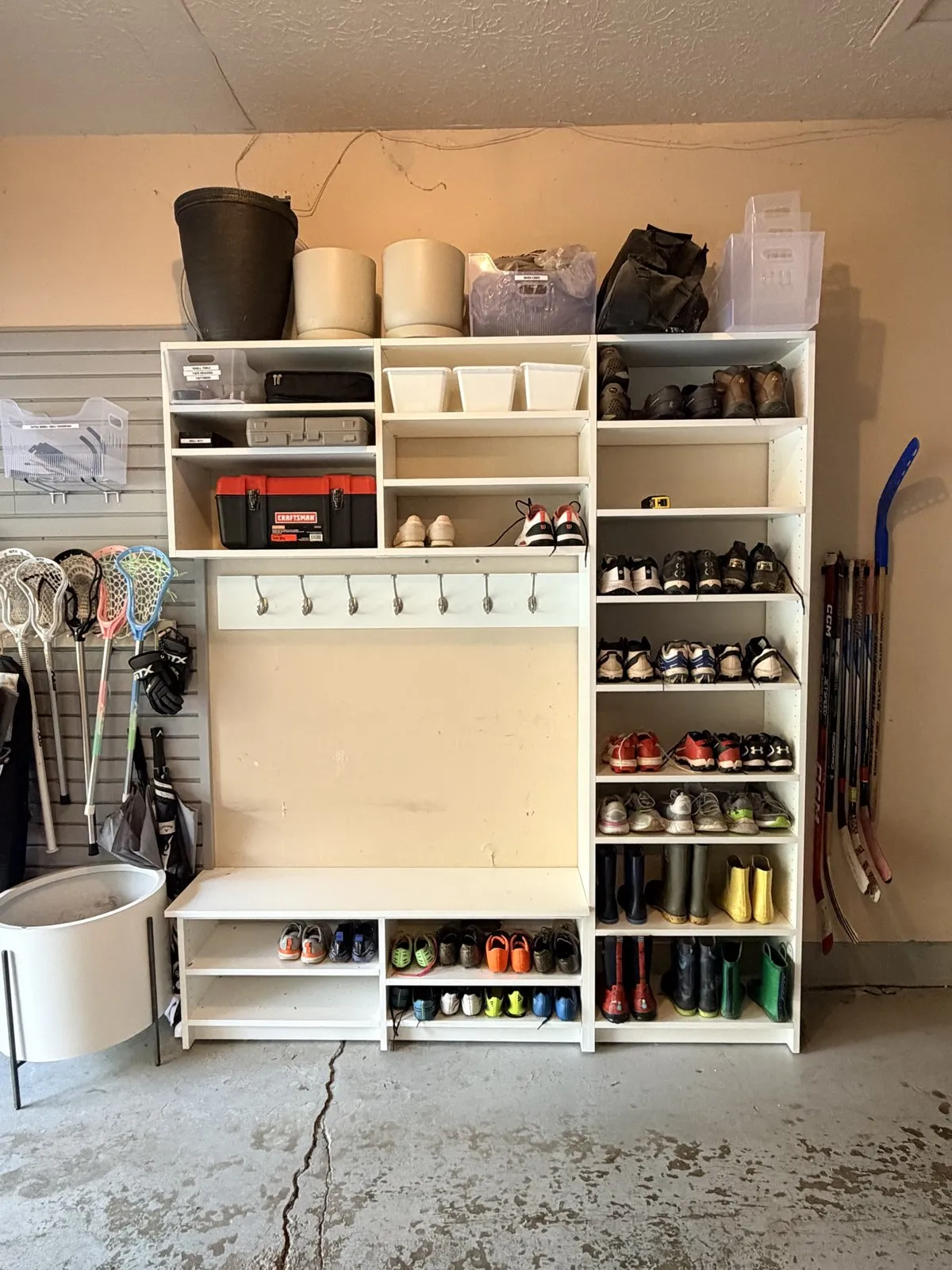 Bench and shoe shelves with cleats and boots sorted by row, lacrosse sticks on the wall