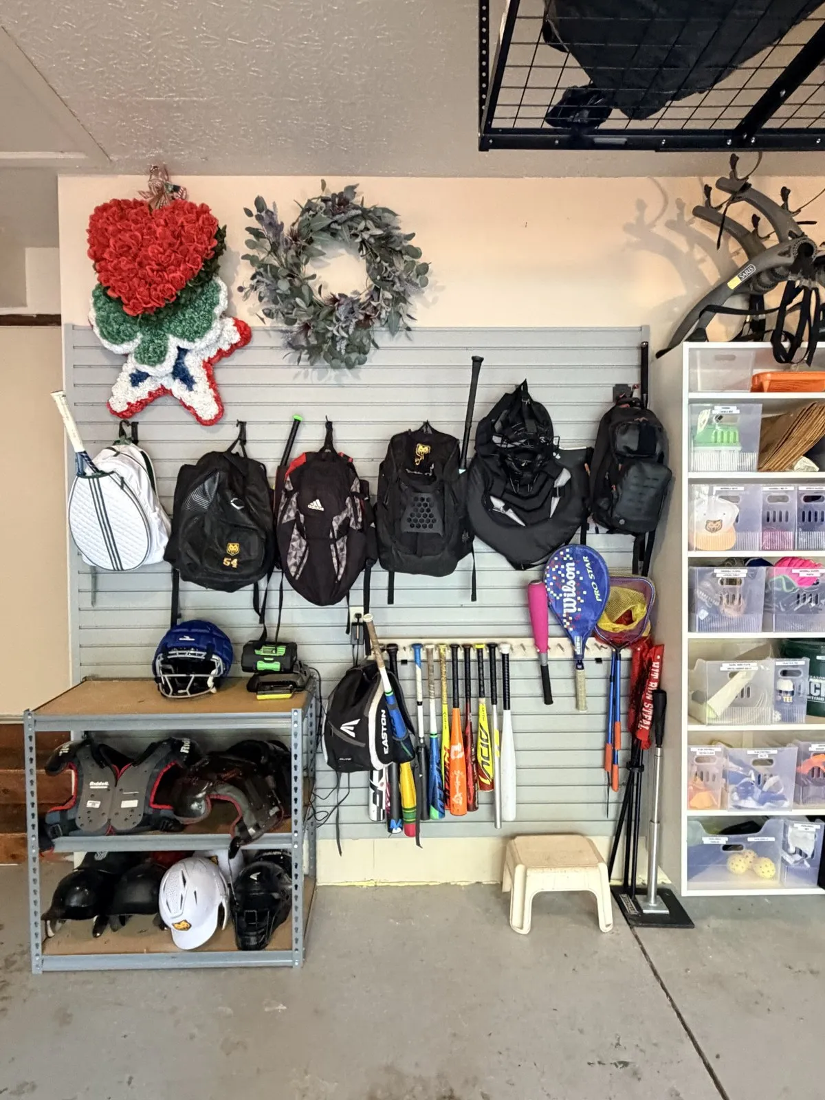 Slatwall with backpacks, bats and rackets hung by type, helmets on a shelf below